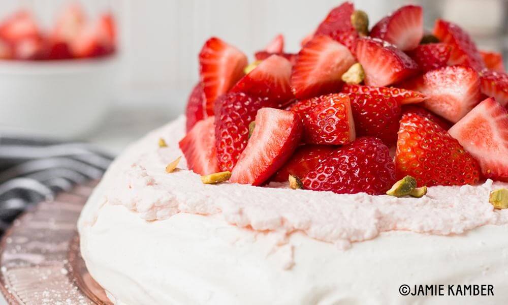 Close Up of Meringue cake topped with fresh pistachios and fresh strawberries.