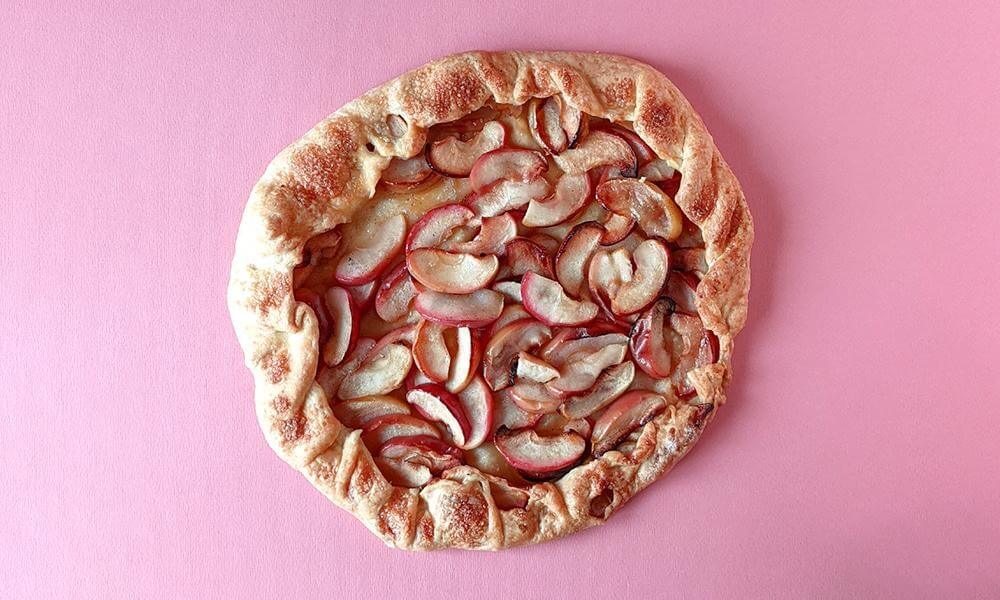 Delicious apple galette pastry on a pink surface.